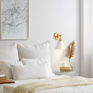 Moti armed sconce with etched glass in brushed gold above a night table by the bed.